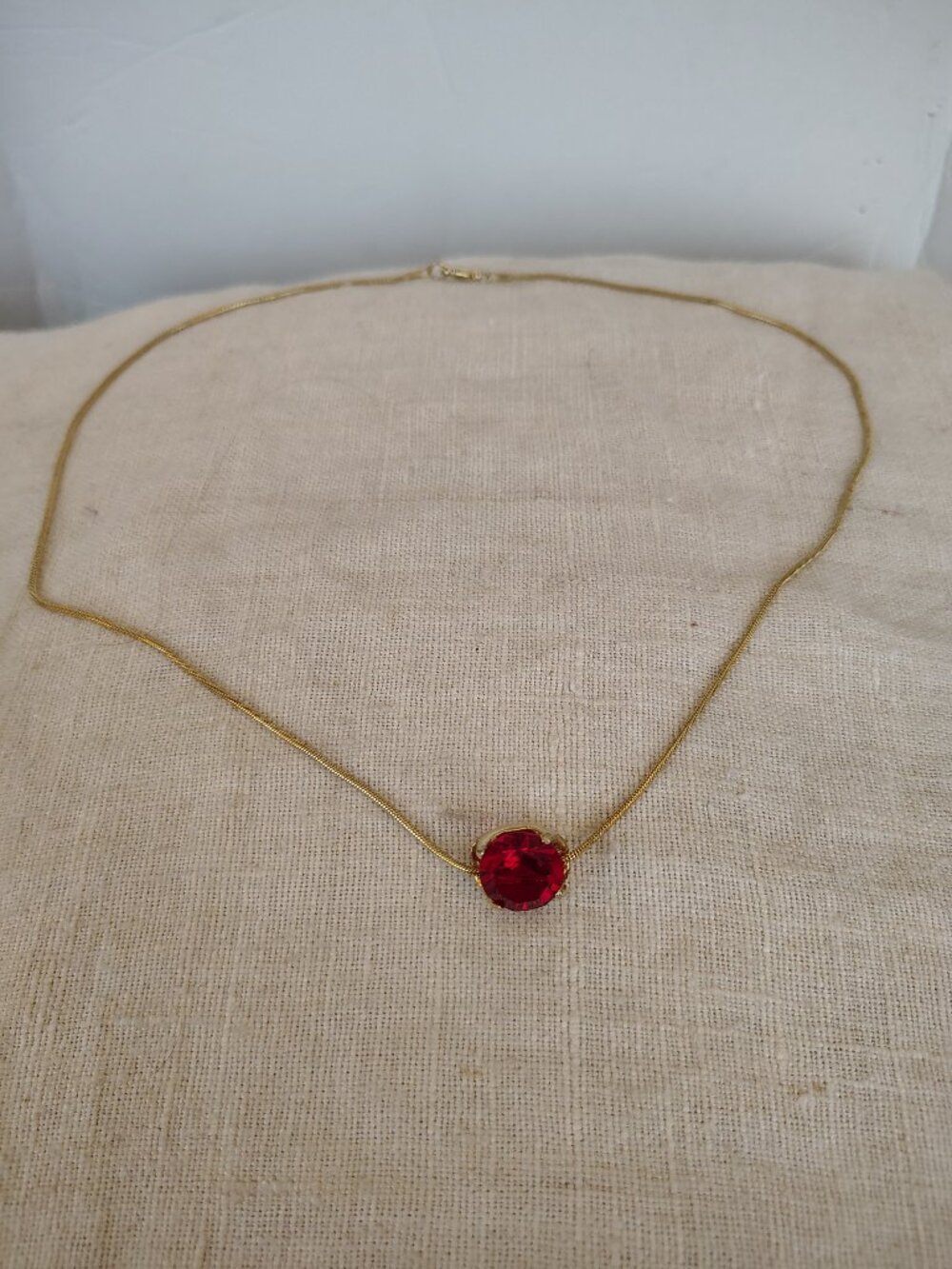 Gold tone pendant necklace featuring a faceted prong mounted red glass stone